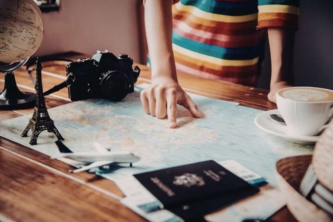 Une personne pointe une carte du monde entourée d'un passeport, d'un appareil photo et d'une tour Eiffel miniature pour la planification d'un voyage à l'étranger.