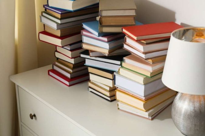 Piles de livres colorés empilés en désordre sur une commode blanche, illustration d'un intérieur qui a besoin de mieux ranger ses livres.