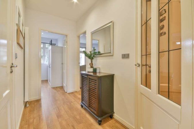 Une petite console noire avec portes persiennes offre une solution de rangement dans une entrée étroite, sous un miroir.