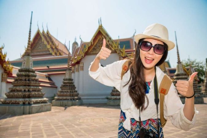 Une touriste souriante fait un geste de satisfaction devant un temple magnifique.