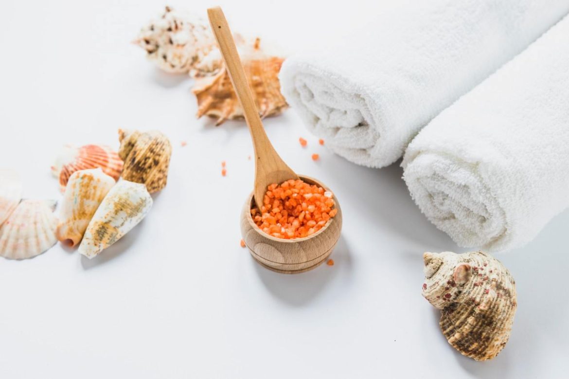Sels de bain marins orangers dans un bol en bois, coquillages naturels et serviettes blanches préparés pour un massage coquillages chauds apaisant.